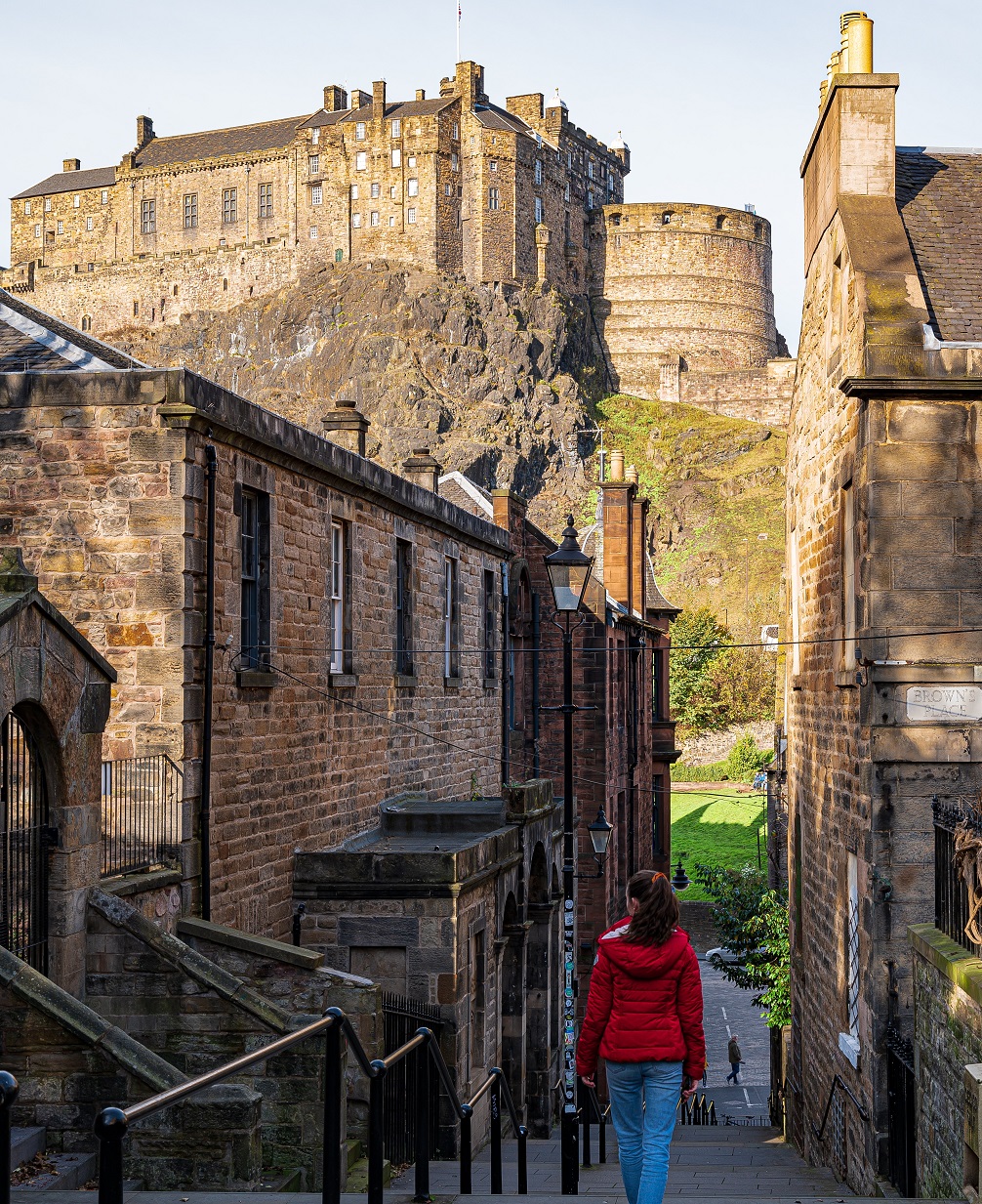 A women walking down a flight of stairs past historic buildings, with Edinburgh Castle in the near distance.